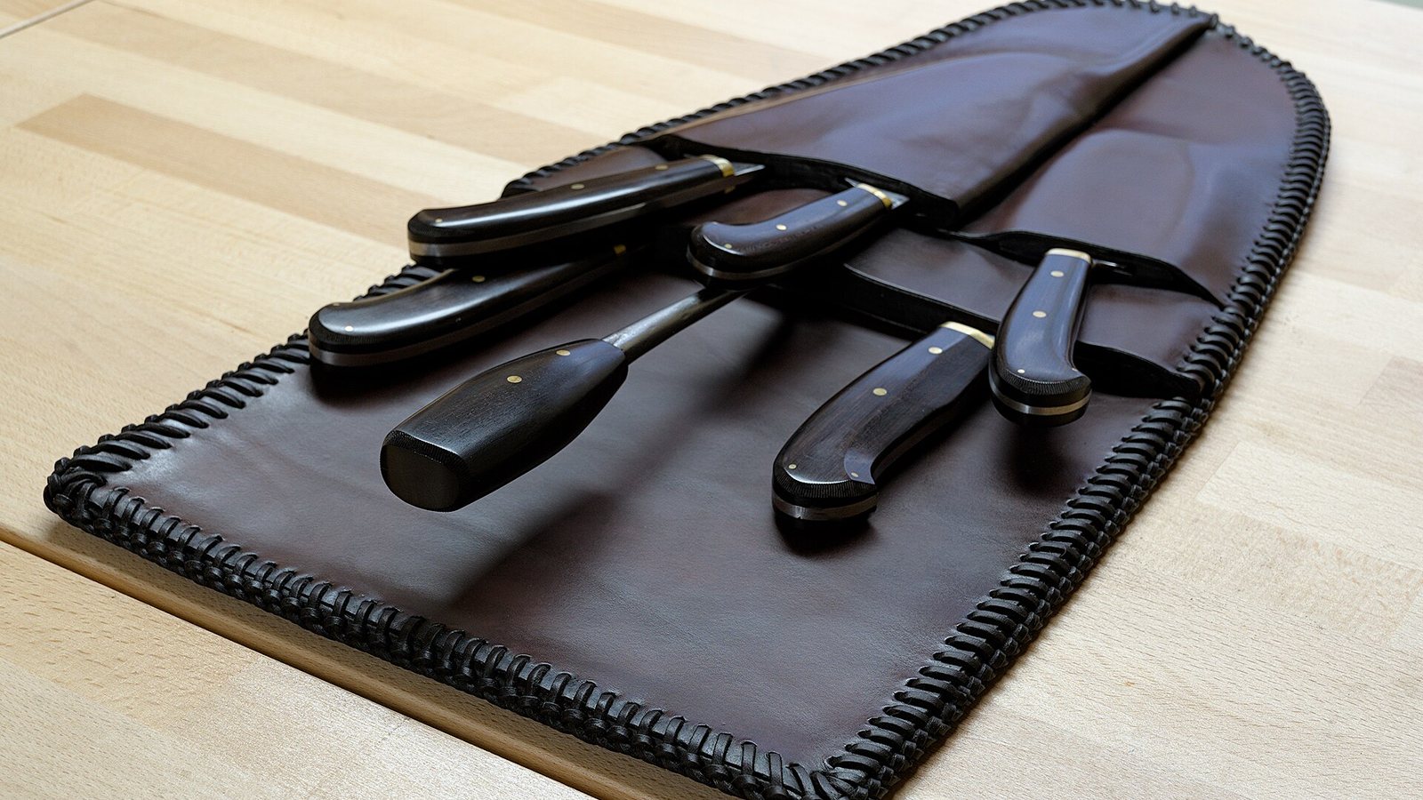 A set of kitchen knives laid out in an open leather knife case