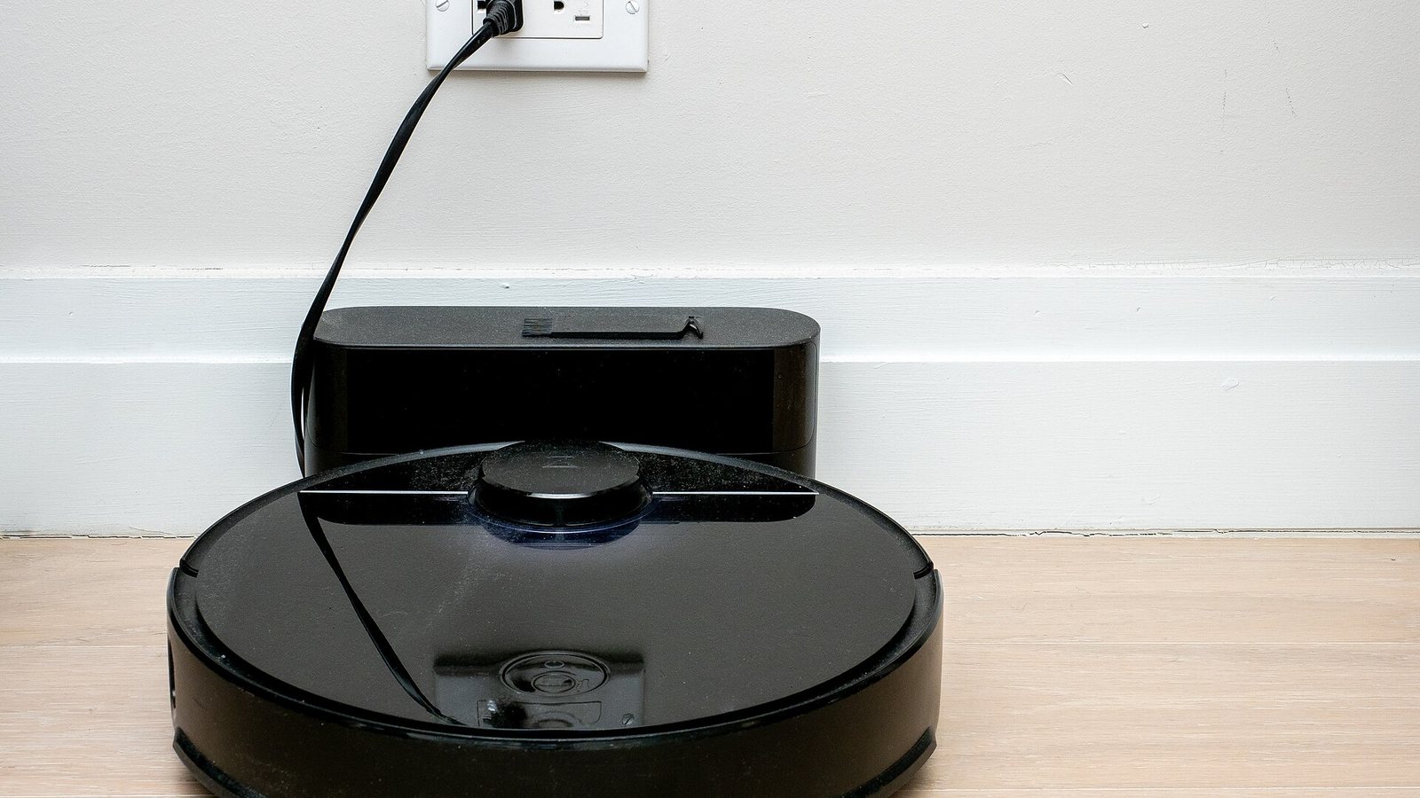 A black robot vacuum parked on its charging dock against a white wall